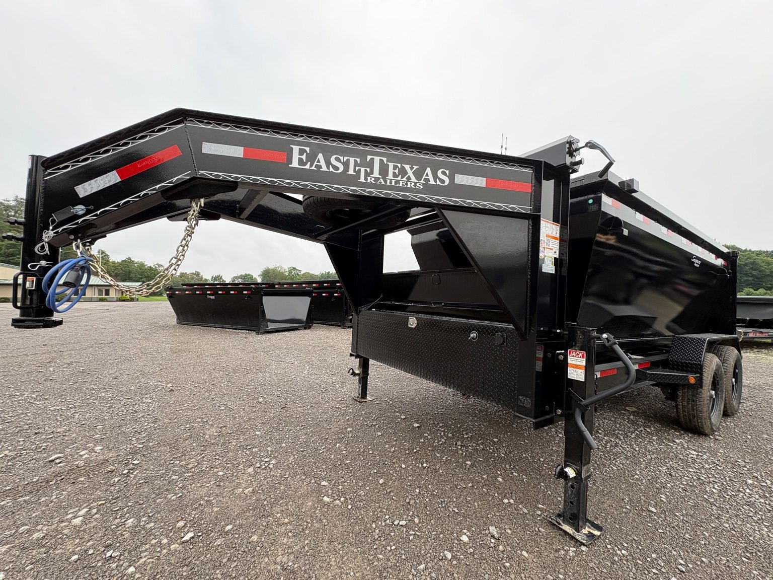 Black gooseneck roll-off trailer set on a gravel lot